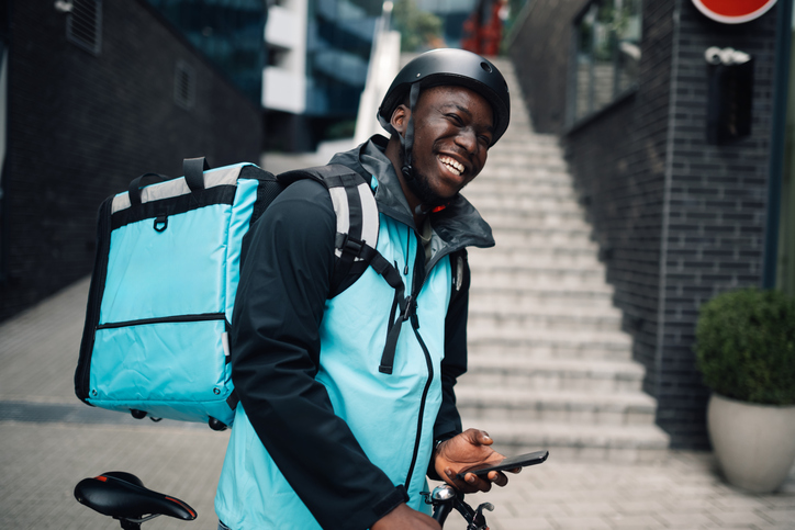 Smiling courier using mobile phone while delivering food with bicycle
