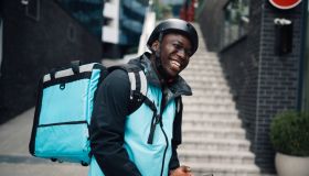 Smiling courier using mobile phone while delivering food with bicycle