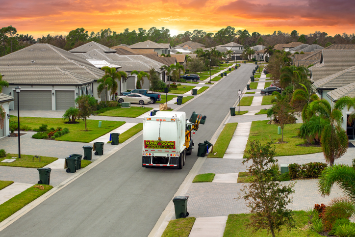 Garbage truck loading trash bin from the curb of American neighborhood