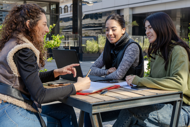 University students collaborating on a project outdoors using laptop