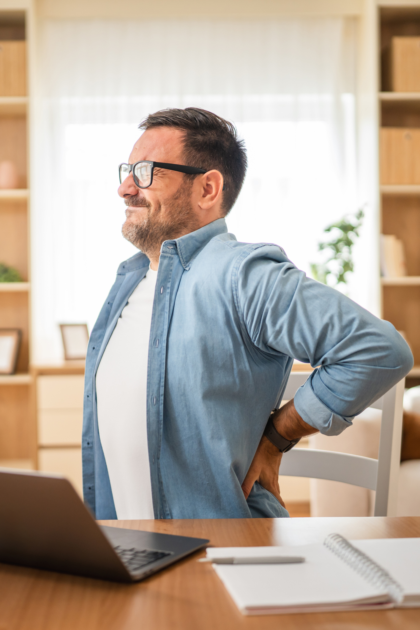 Man working from home suffering from back pain while using laptop