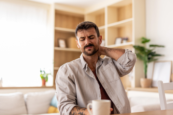 Man experiencing neck pain while sitting at home