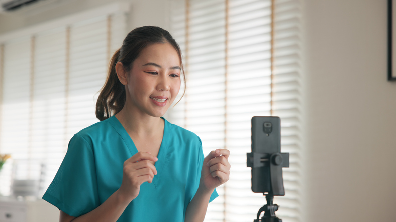 Young adult woman Gen Z asia people anti aging expert modern nurse live talk viral video selfie camera on mobile phone app mental health care. Online sharing digital virtual asian vlogger filming.