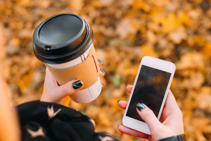 Close-up of a paper cup with coffee and a cellphone in the hands