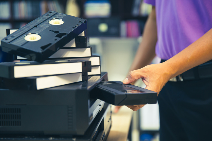 Close-up hand chooses and put or insert video cassette tape VHS old retro style on video record playback concept of vintage electric and electronic appliances multimedia player device old fashioned.