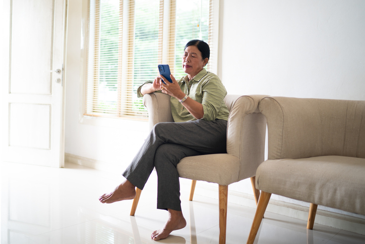 Woman sitting relaxed on sofa using mobile phone at home