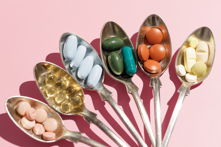 Various of spoons with pills and tablets on the pink background