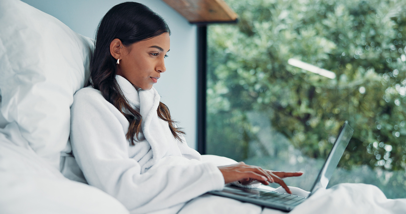 Woman, typing and remote work in bed with laptop for email feedback, administration and calendar. Freelancer, person and pajamas in home with computer for daily update, schedule and project review.