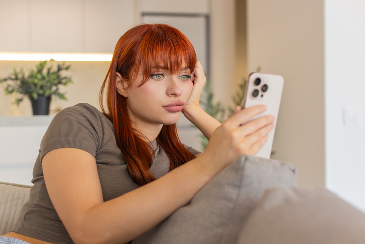 Young woman tires of endless news feed on smartphone bored annoyed low energy and mental drain mood