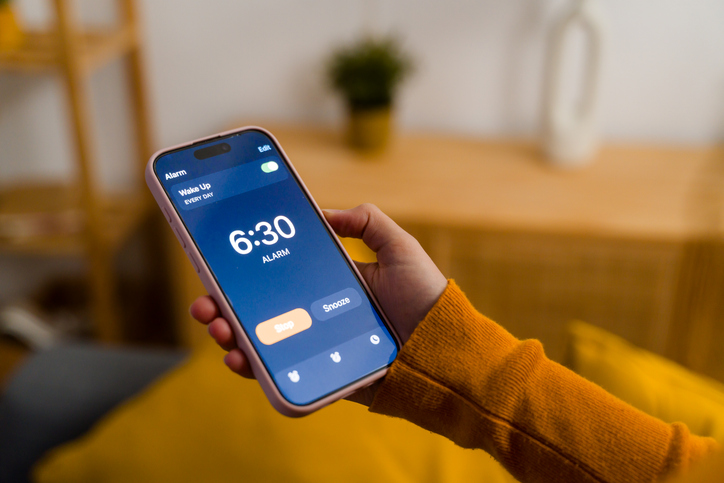 Hand holding smartphone displaying alarm set for 6:30 AM