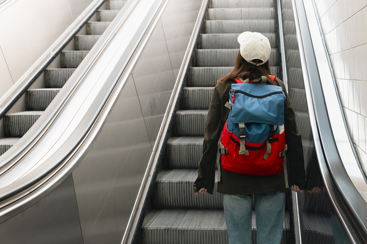 Young woman with a backpack on an escalator at a railway station, highlighting modern travel and transit infrastructure.