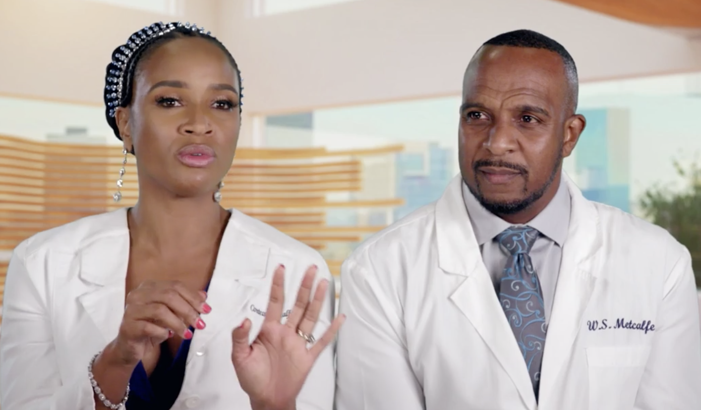 Two people in white lab coats, one wearing a headpiece, standing in a medical setting.