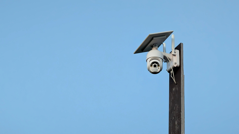 Modern surveillance camera mounted on a pole with solar panel against a clear blue sky, representing smart security technology, monitoring systems and sustainable infrastructure.