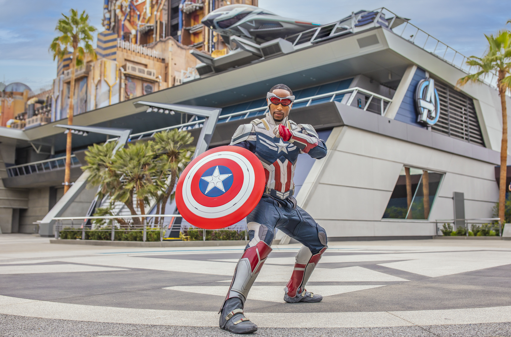 A person dressed as Captain America stands in front of the Avengers Campus at Disney California Adventure Park, holding up his iconic shield.