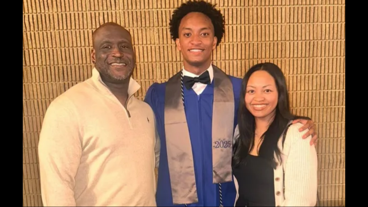 Three people smiling together in formal attire, with the middle person wearing a graduation gown and cap.
