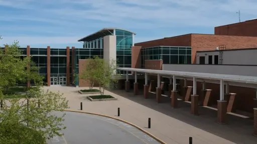 A large brick and glass building with a covered entrance and parking lot in front.