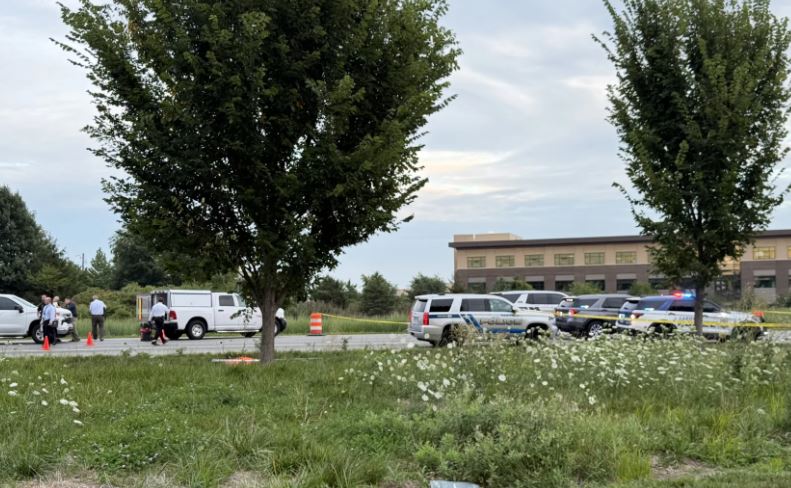 A grassy field with trees, police vehicles, and people standing near a building.