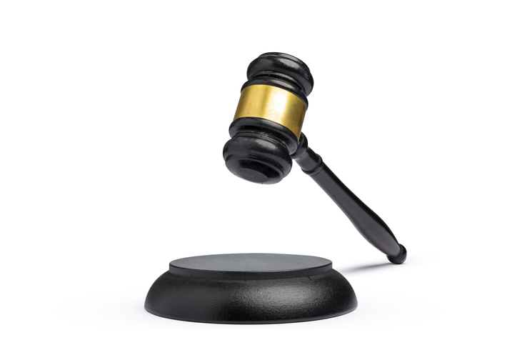 Black wooden judge gavel with brass accent hovering above its sound block, isolated on a white background. Law, justice, and order concept.